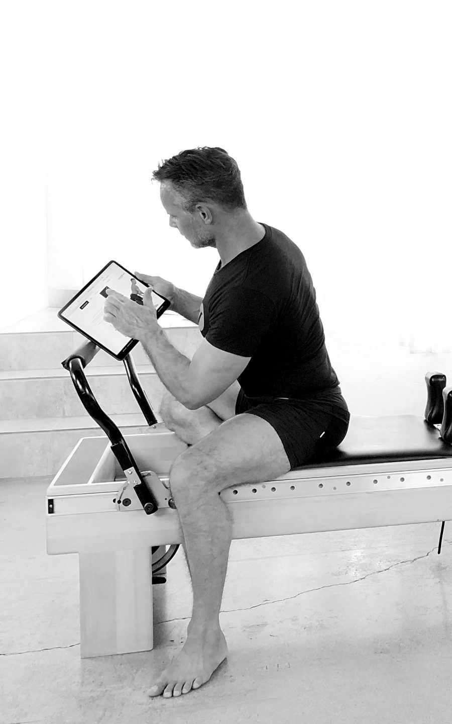 Sean on a pilates machine reading something on a tablet